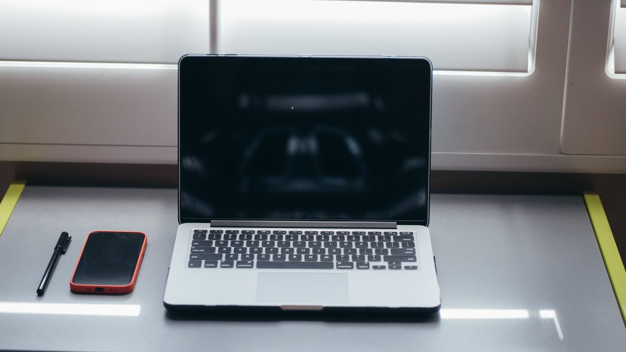 A laptop and smartphone arranged on an empty desk by a window